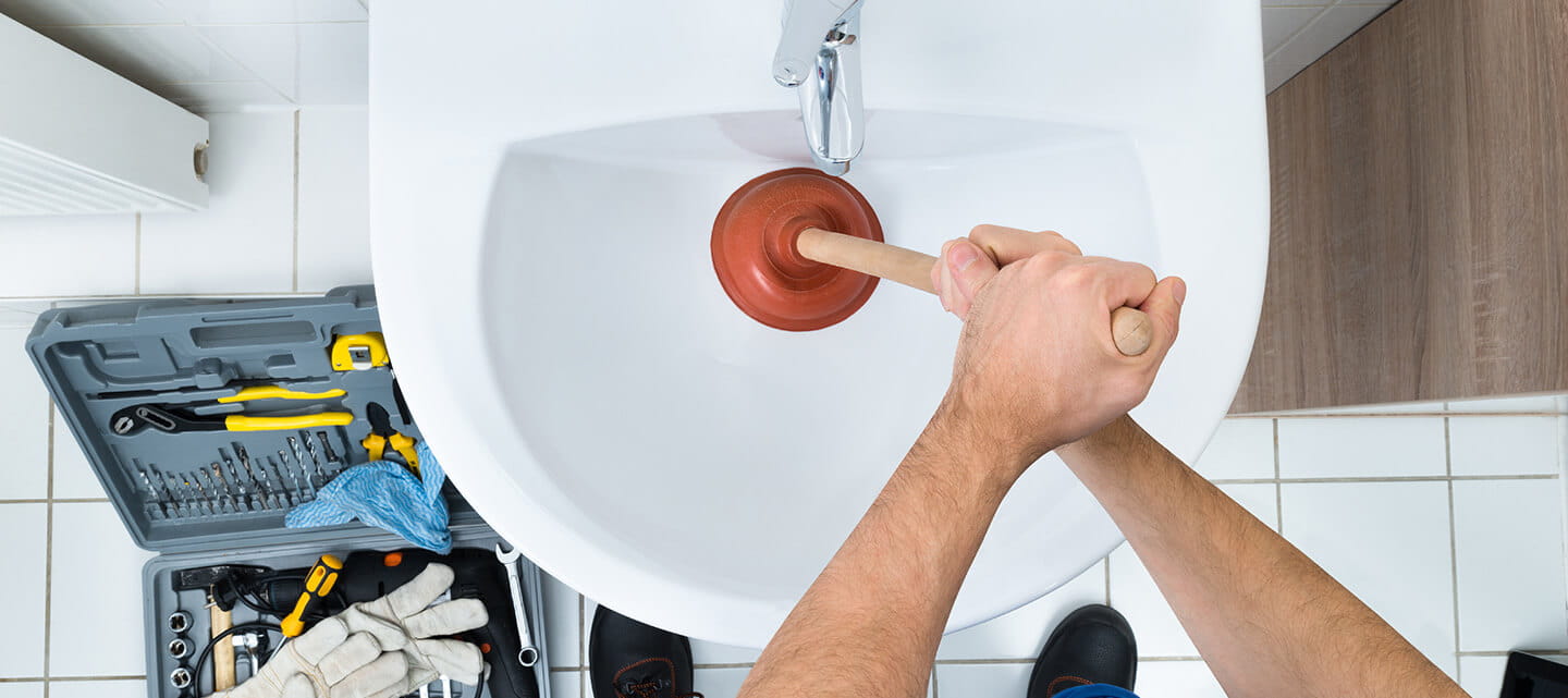 Close up aerial view of a plumber using a plunger on a sink