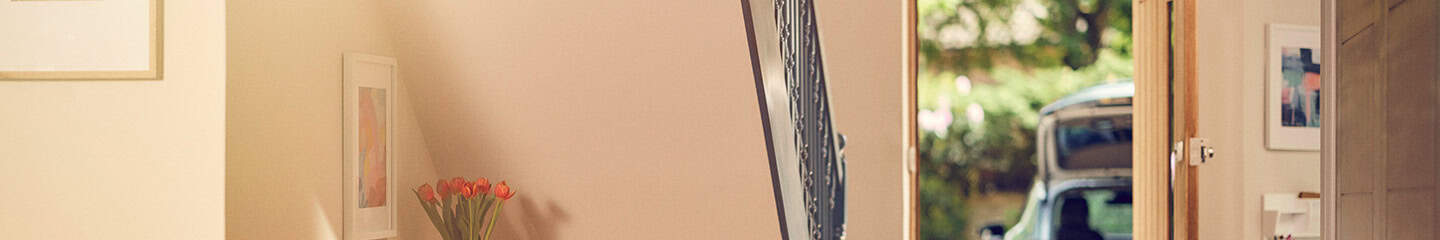 Interior view of an empty hallway with the front door open, through which you can see a parked car with the boot oprn.