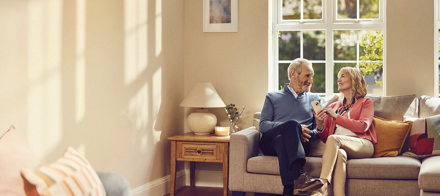 A happy mature couple enjoying what they see on their phones while sat together in their living room