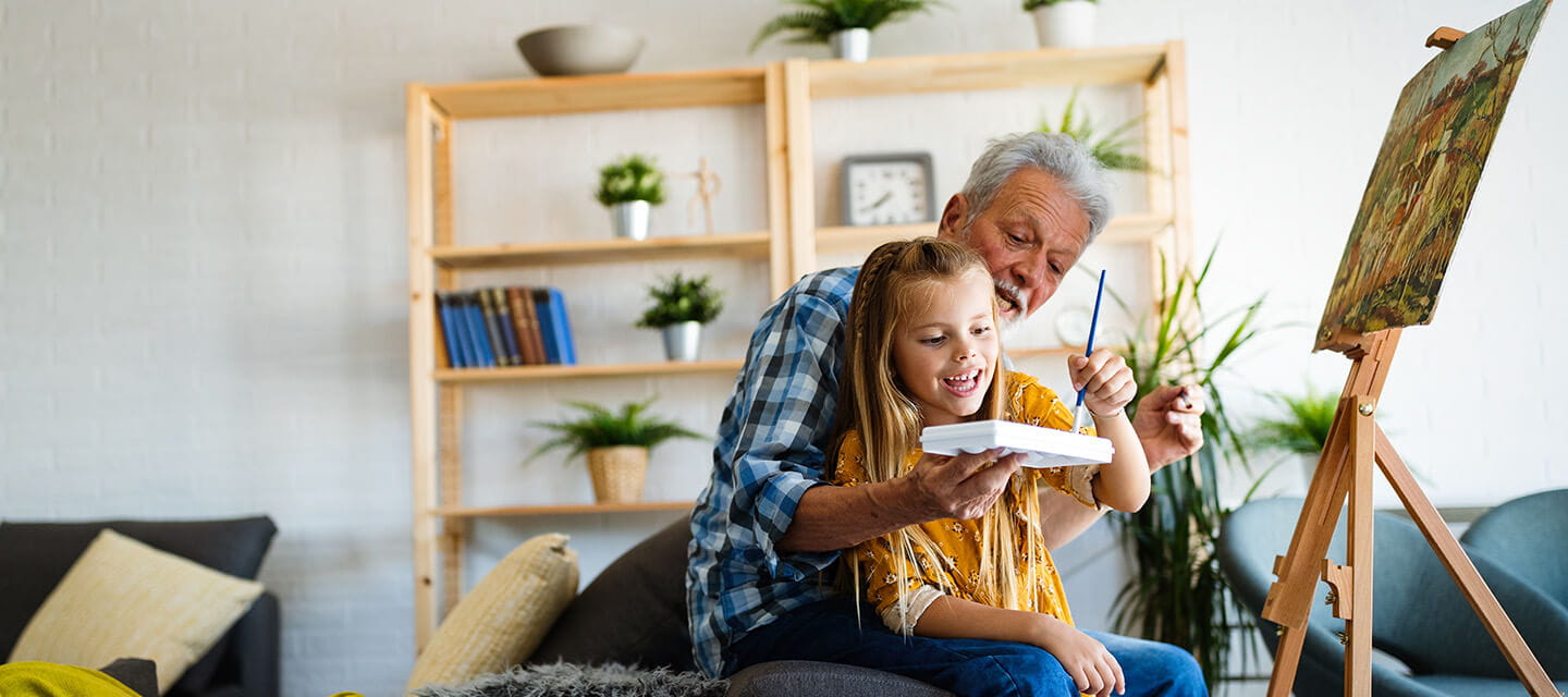 Senior man with child painting on canvas. Grandfather spending happy time with granddaughter