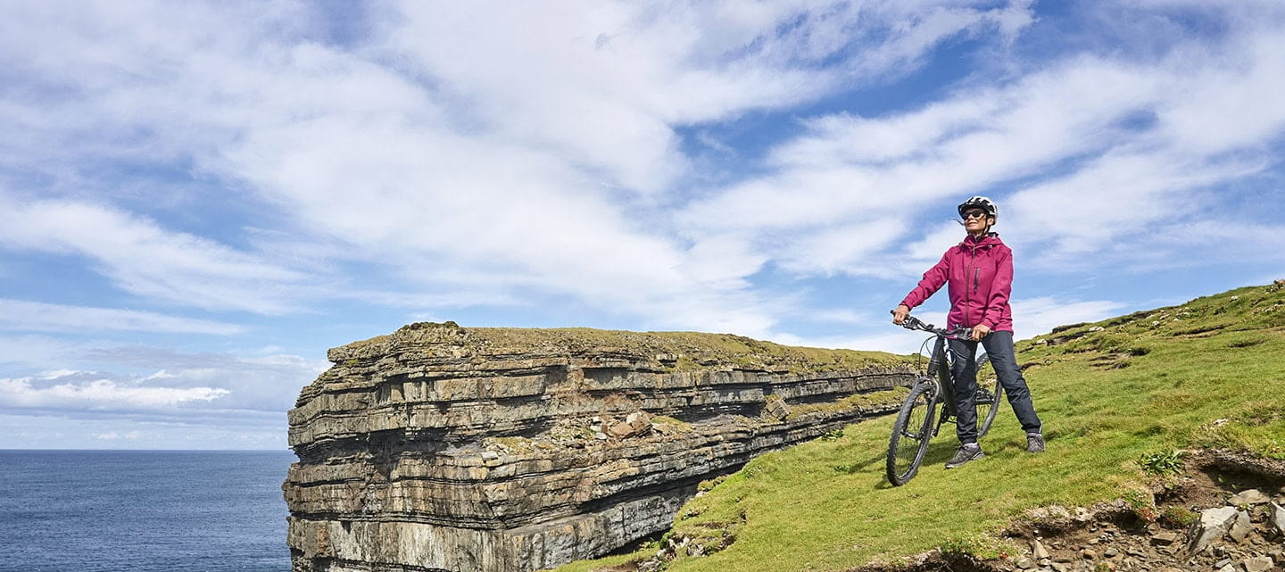 A mature cyclist, taking in the view from the edge of a cliff on a sunny day.