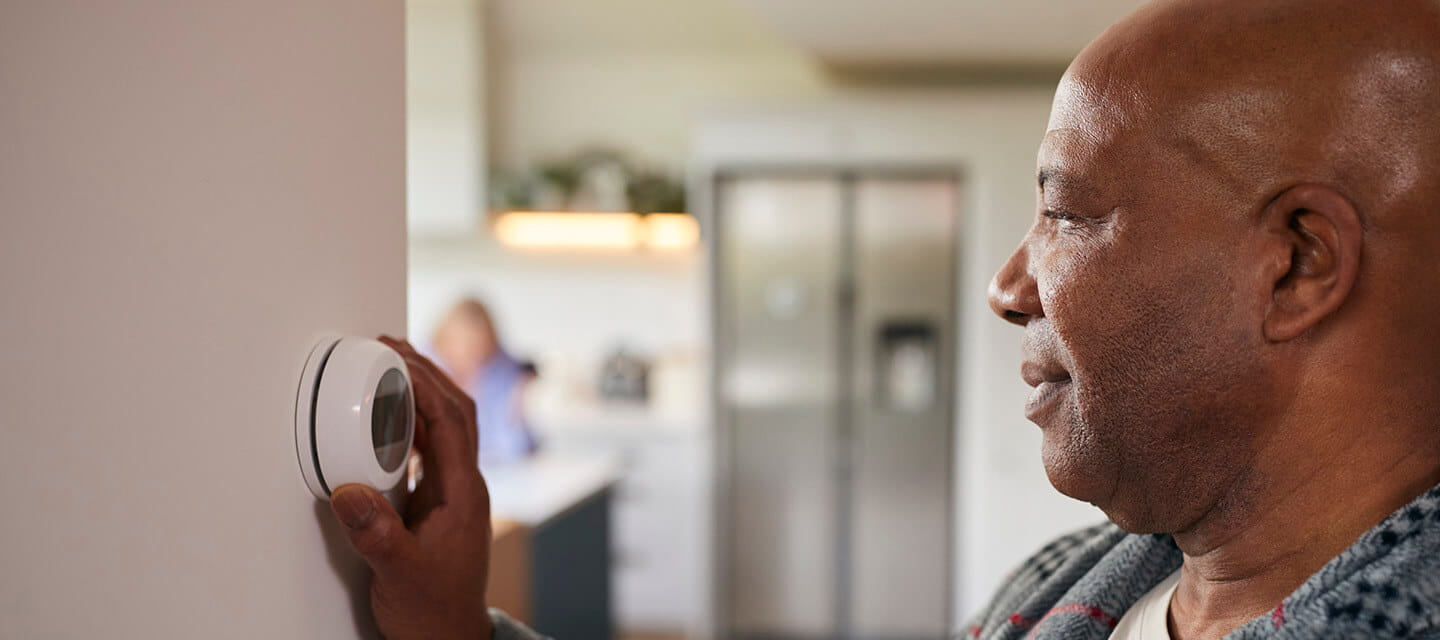 Mature man turning control dial on digital central heating thermostat at home