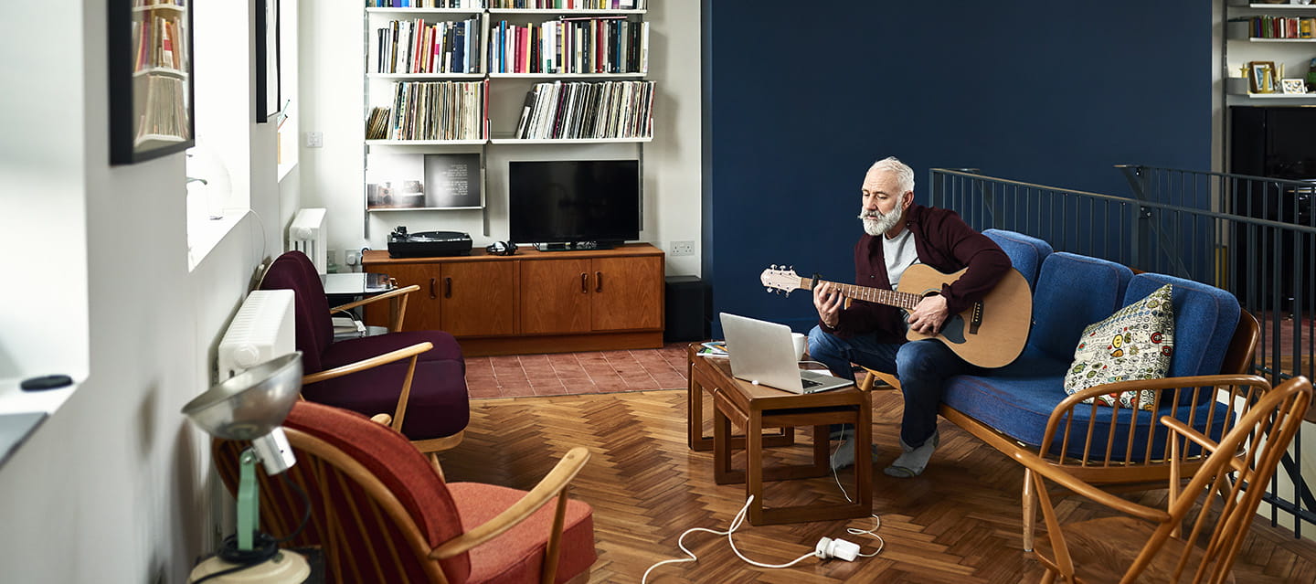 Senior man practising guitar at home in retro living room