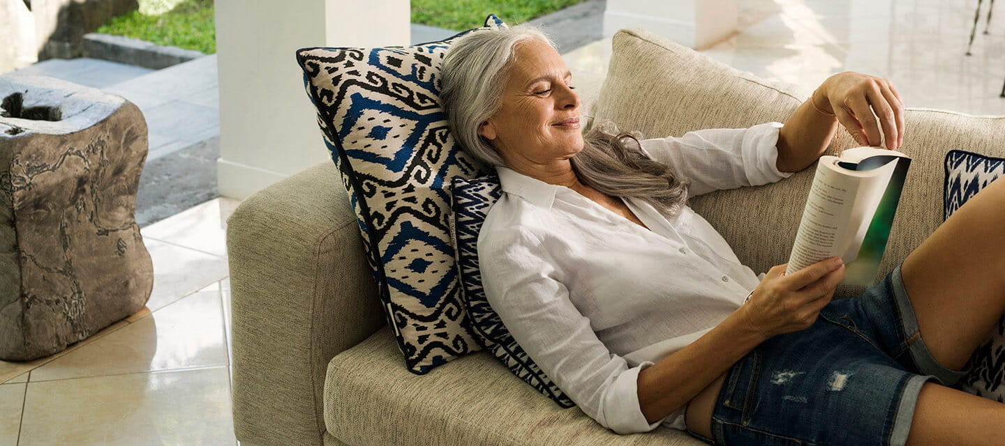 Elegant senior woman relaxing on couch, reading a book