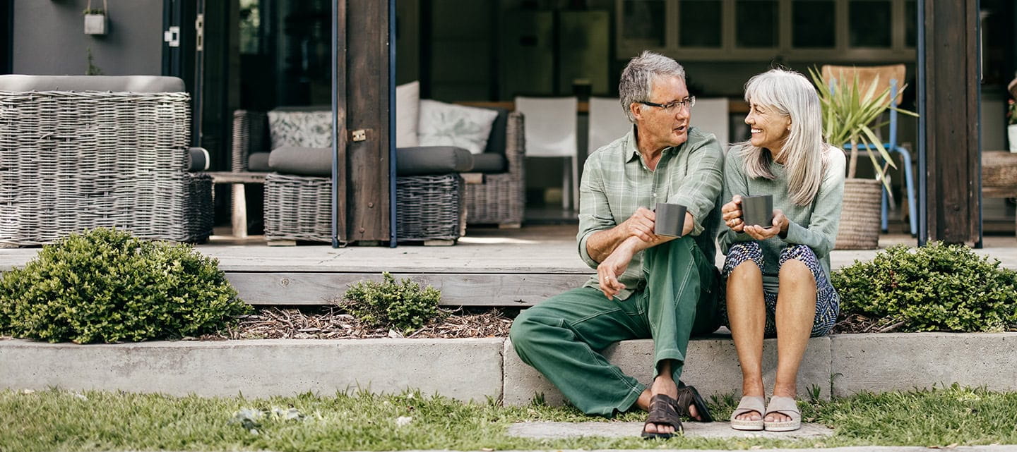 Seated outside their home, a couple in their 60s have a conversation in the fresh air.