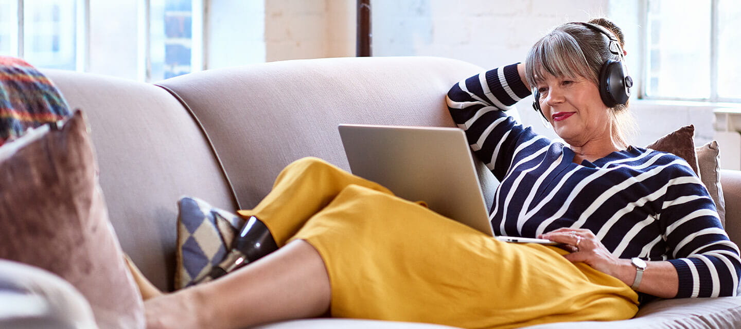 Senior woman wearing headphones watching movie on laptop