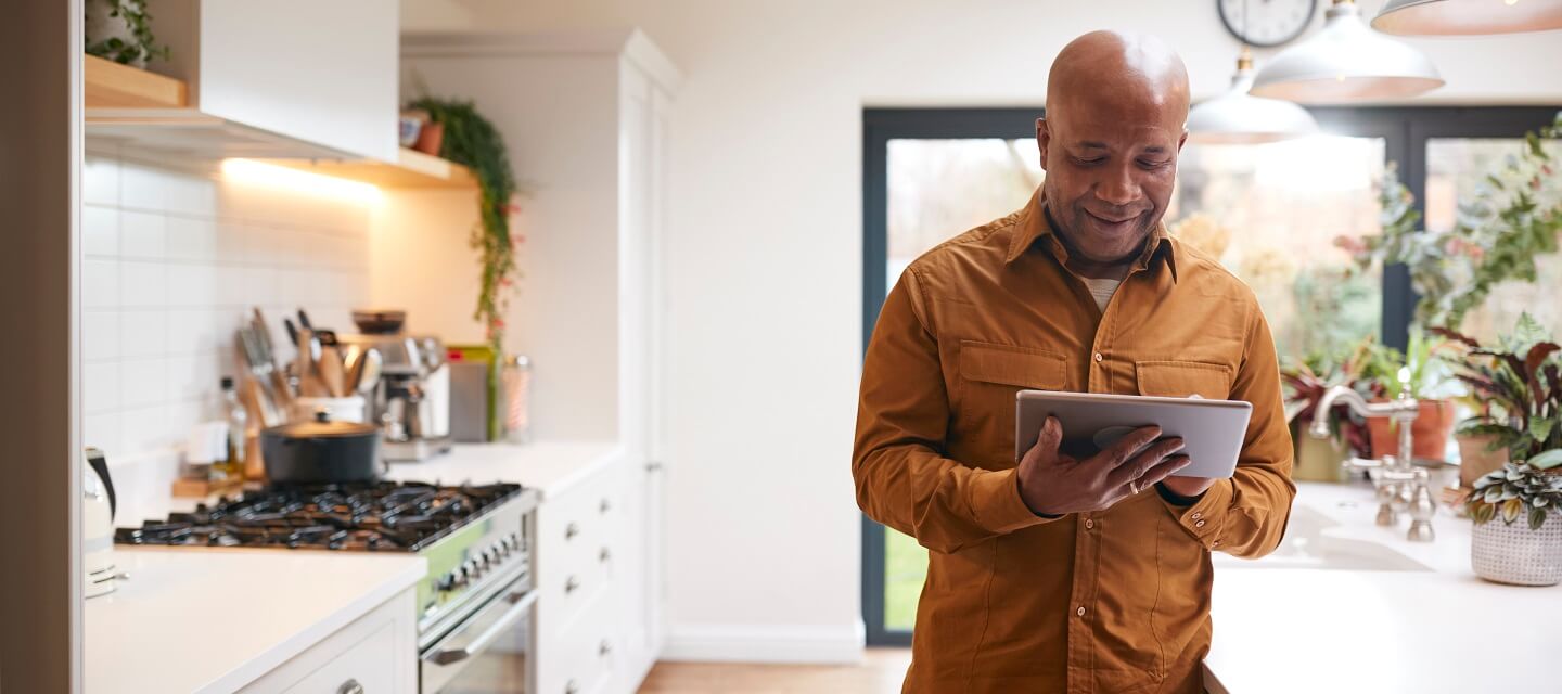 A man stood in his kitchen looking at his tablet computer