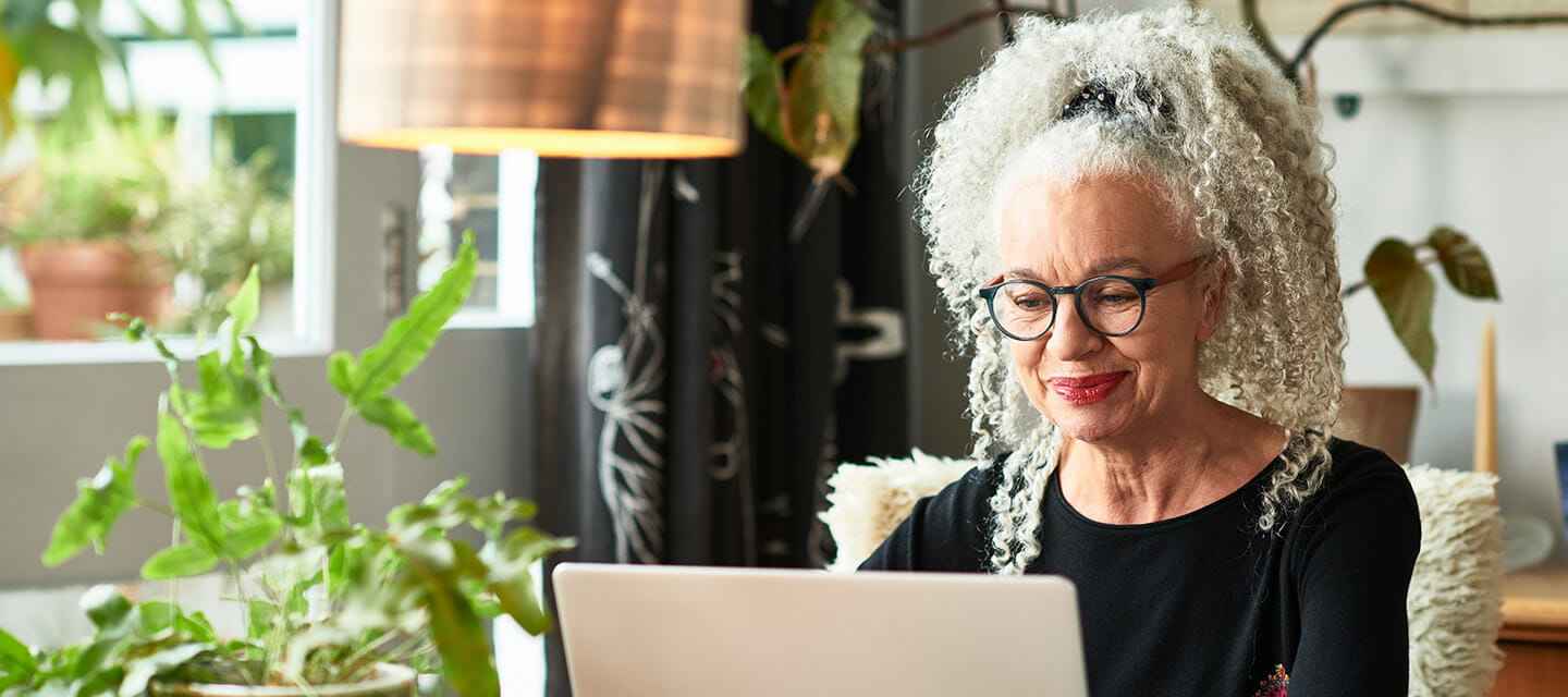 Grey haired woman at home smiling in front of laptop