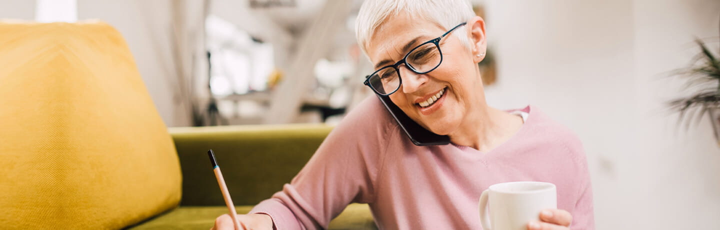 A mature woman talking on her mobile phone while making notes