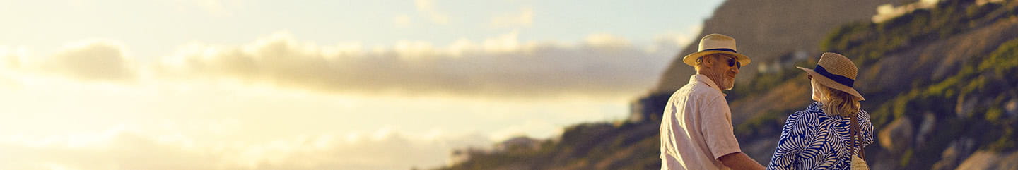 A mature couple walking along a sandy beach as the sun sets