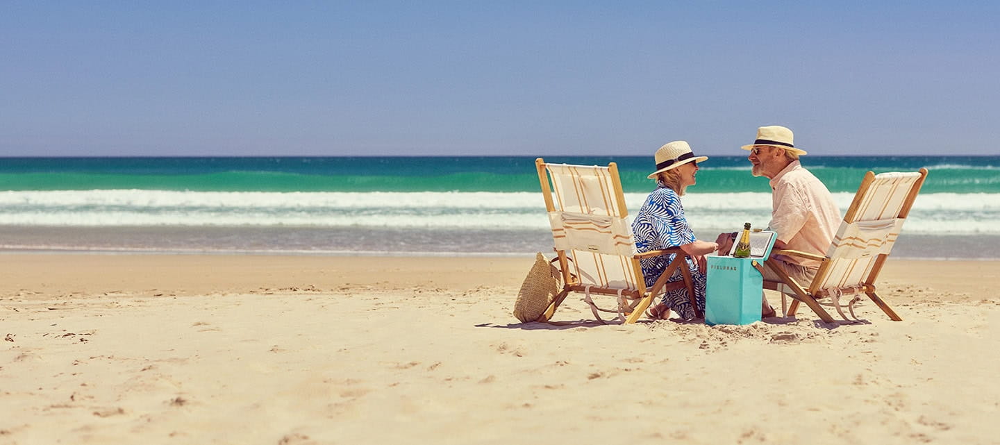 A happy mature couple relaxing by the sea on deck chairs with a bottle of champagne.