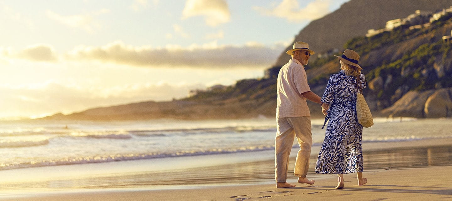 A mature couple walking along a sandy beach as the sun sets