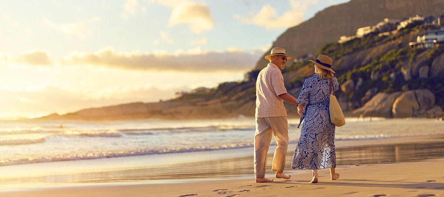 A mature couple walking along a sandy beach as the sun sets