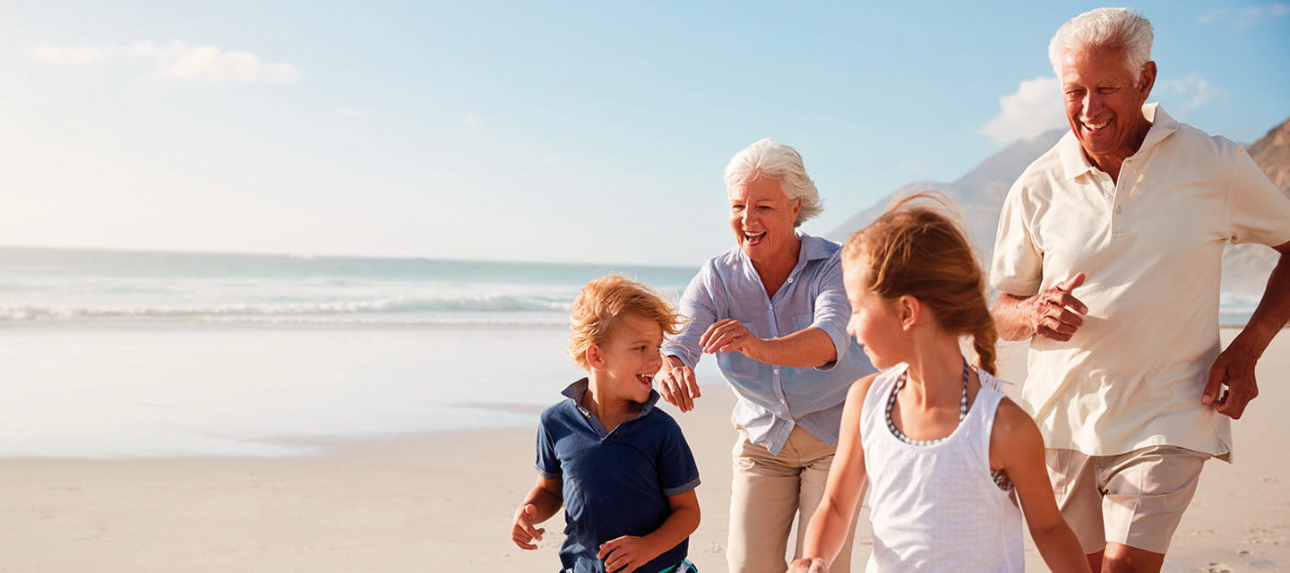 Grandparents running with their grandchildren along a sunny beach
