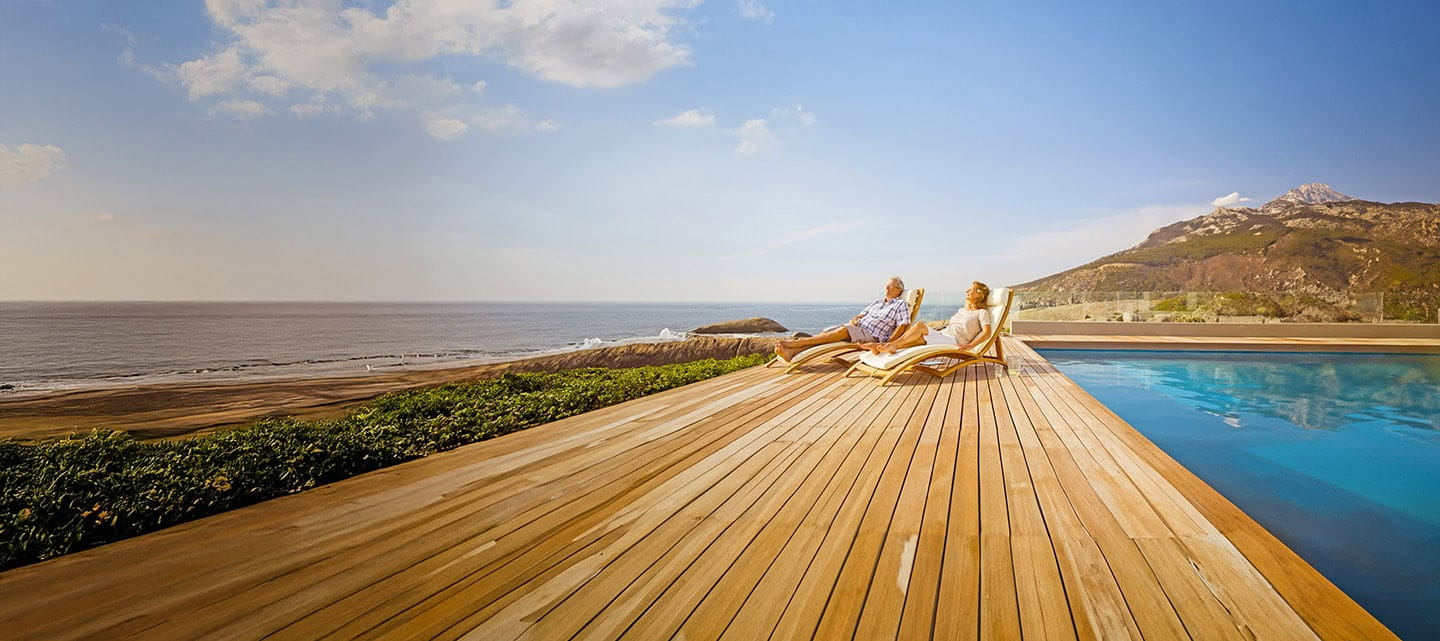  Older couple enjoying a sunny day relaxing on sunloungers by a swimming pool. 