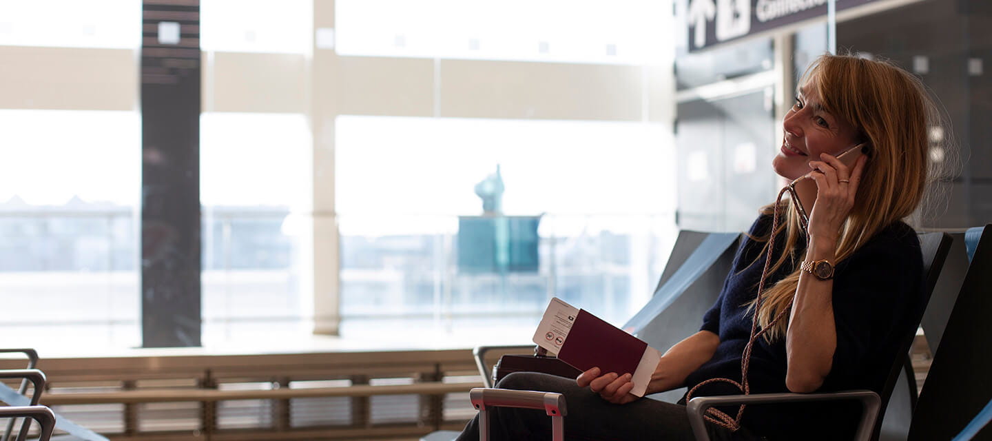 A mature woman on the phone sitting in an airport departure lounge