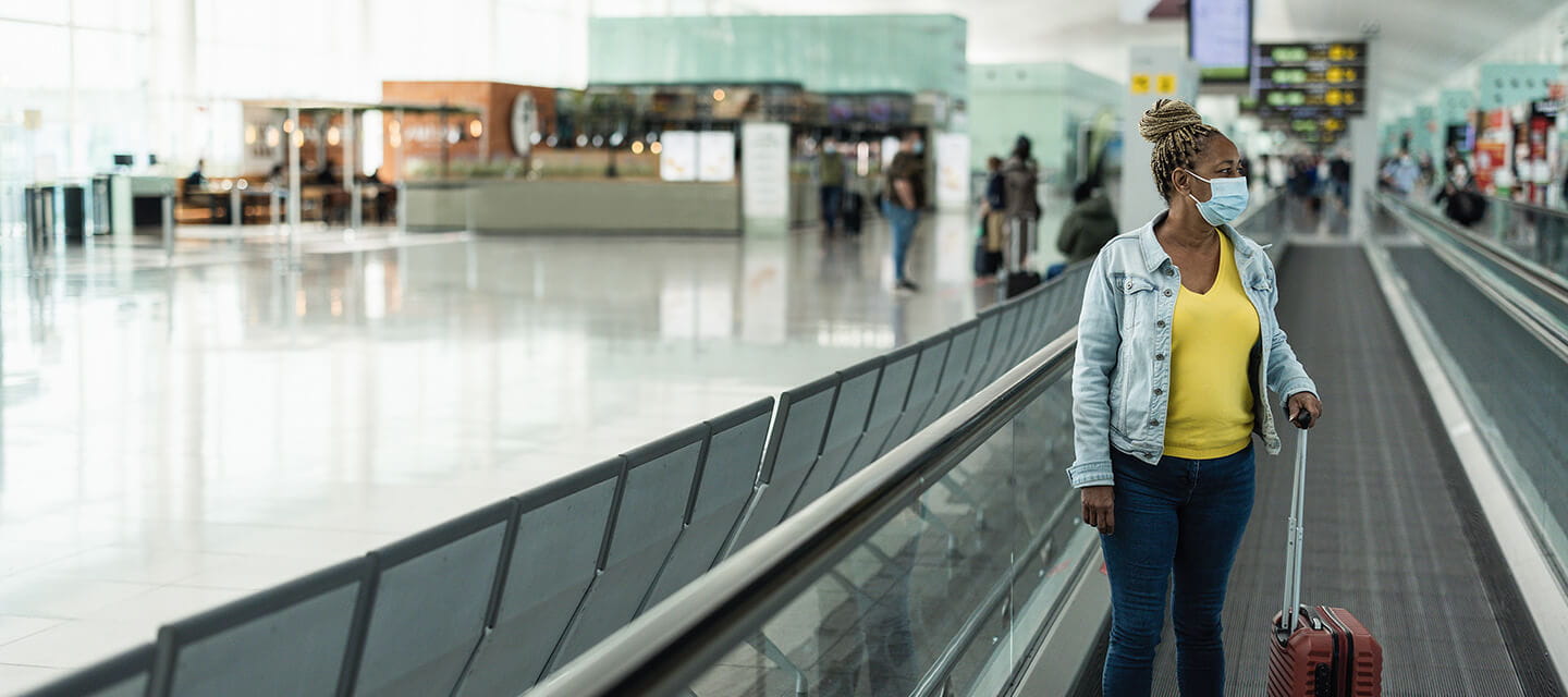 Senior woman using moving walkway inside terminal airport with face mask