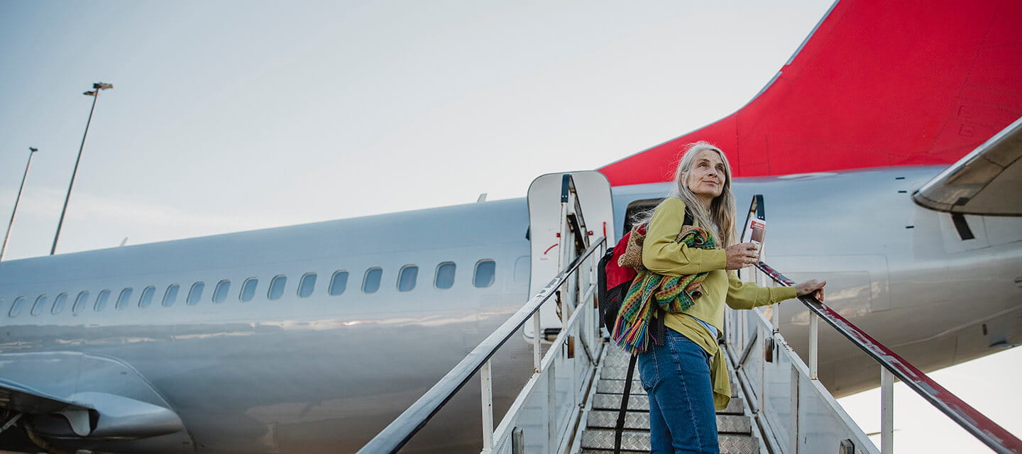 Mature woman is standing on the air-stair of her plane with her boarding pass and has turned round to give one last look to her home before she goes travelling.