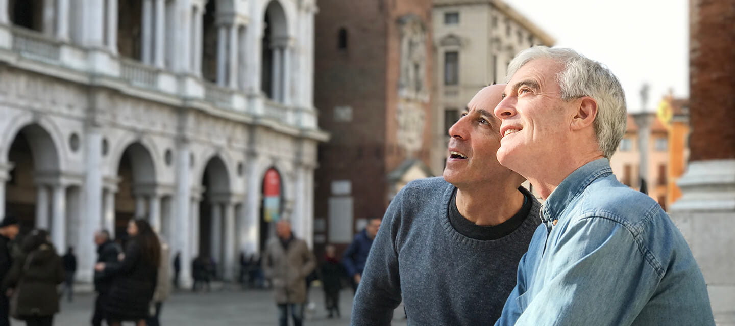 Two men sitting on steps of a historic building and looking up at the architecture