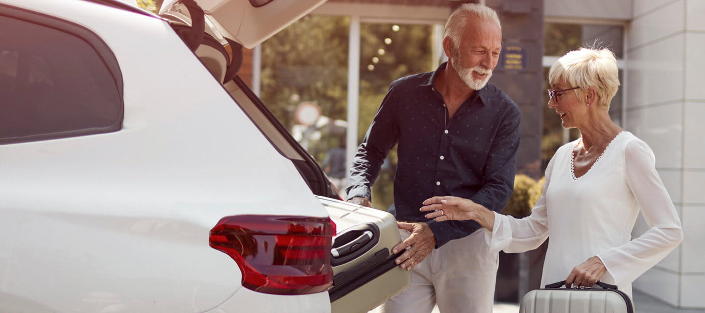 A mature couple packing luggage in their car at a hotel