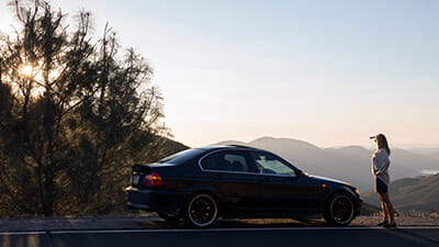 Woman stands beside parked car, looks across hills