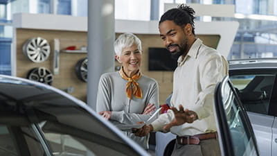 Happy salesperson showing car to customer in showroom