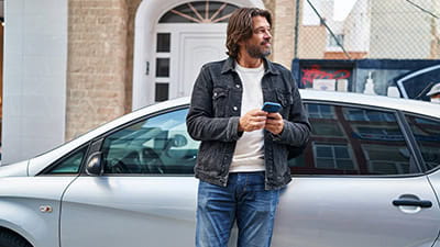 Middle age man using smartphone leaning on car at street