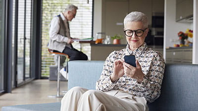 Senior woman sitting on couch at home using mobile phone