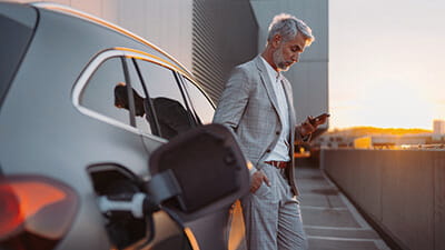 A man looking at his phone while his electric car charges