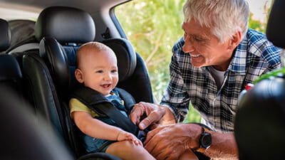 A grandparent plugging their grandchild in to a child car seat