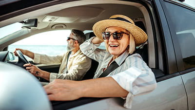 Senior woman leaning through car window while enjoying ride with her husband.