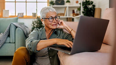 Mature woman using laptop on living room floor with wireless headphones