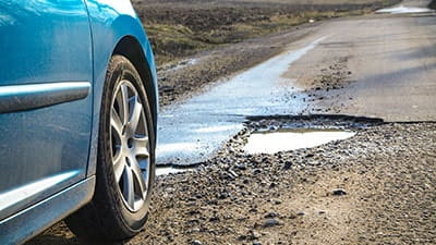 Car parked near a big pothole on an empty road