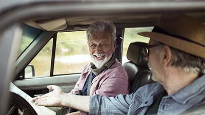 Two men laughing while reading a map in their car