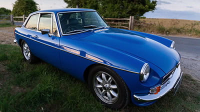 A bright blue British classic car, is parked up off road.