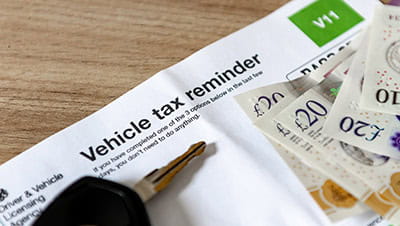 A vehicle tax reminder document of a desk with car keys and money.