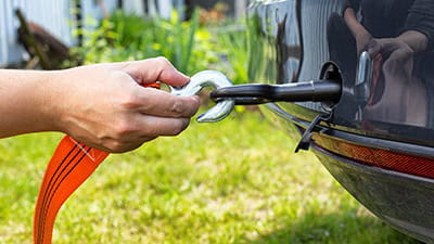 A hand attaching a car tow hook with an orange tow rope for towing.