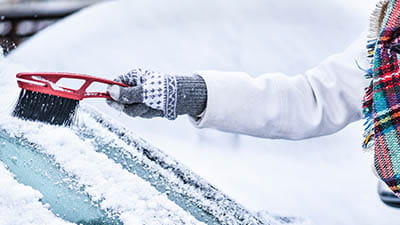 A woman scraping snow and ice from their car windscreen