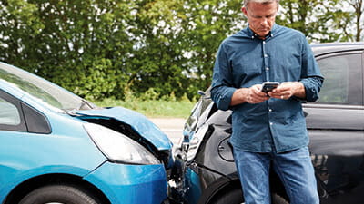 A man standing by 2 cars that have crashed