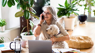 A mature woman on the phone smiling while holding her pet dog