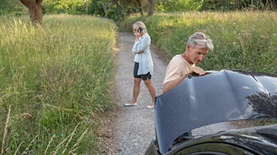 Mature woman calls for help while a mature man checks out issues with a car engine on a rural road
