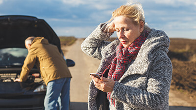 A woman calling for assistance while a man looks under a car bonnet
