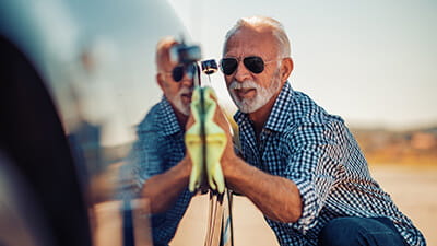 A mature man in sunglasses waxing his car