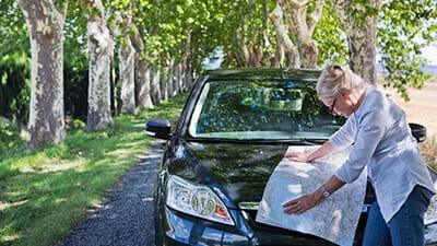 A mature woman reading a map of Europe on the bonnet of her car