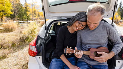 Happy, affectionate senior couple playing ukulele at back of car 