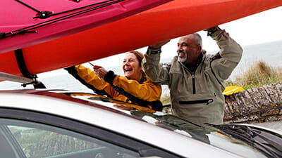 Mature couple securing kayaks to car