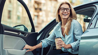 A smiling mature woman leaving her car with a takeaway coffee