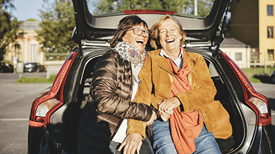 Two ladies sitting on the edge of a car boot laughing