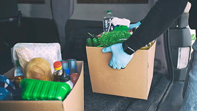 A volunteer removing a box of groceries from the back of a large car