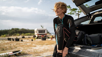 Mature female surfer getting dressed in shoes and wetsuit before going surfing